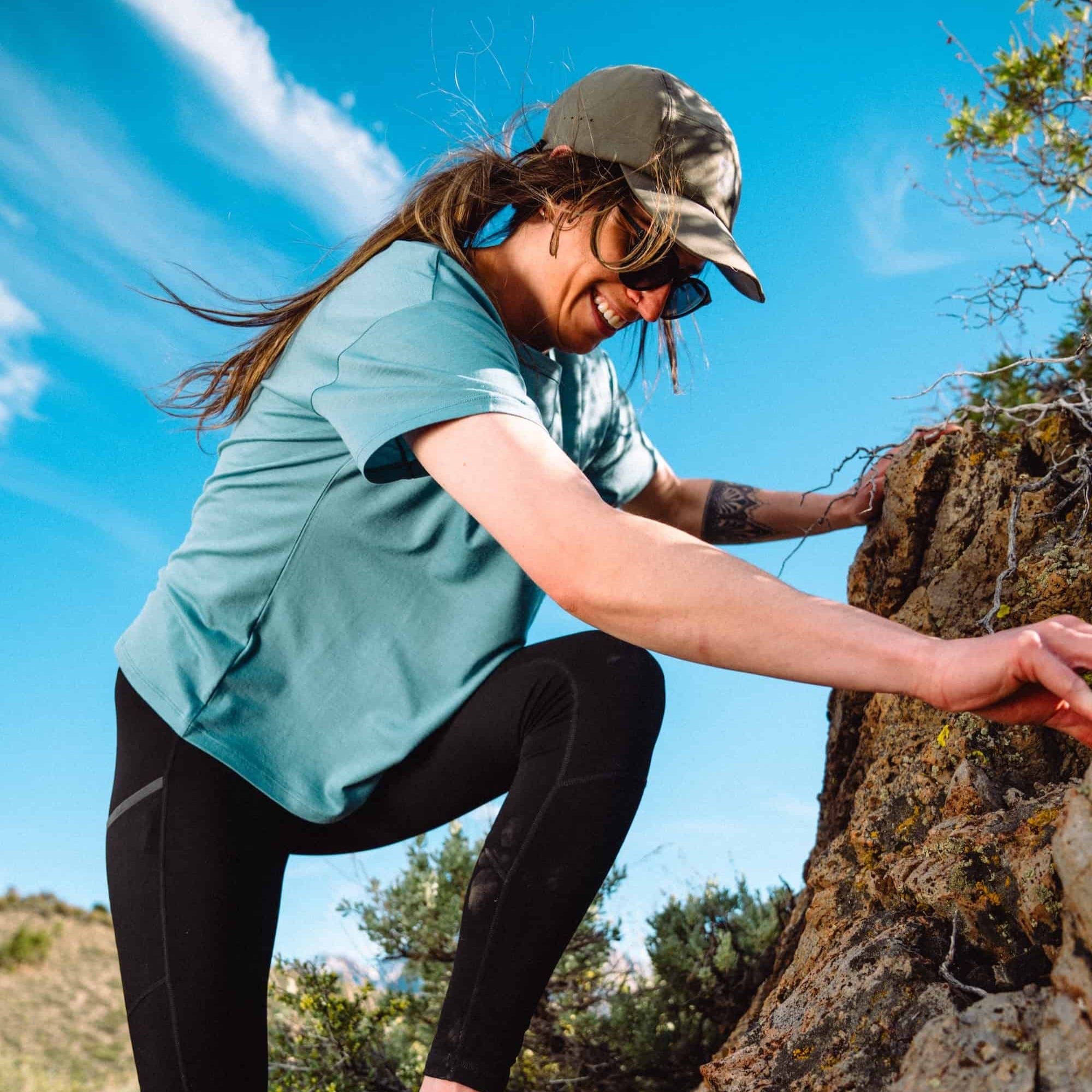 a woman scrambling on a rock wearing a Journey Relaxed Fit Tee in Smoke Blue