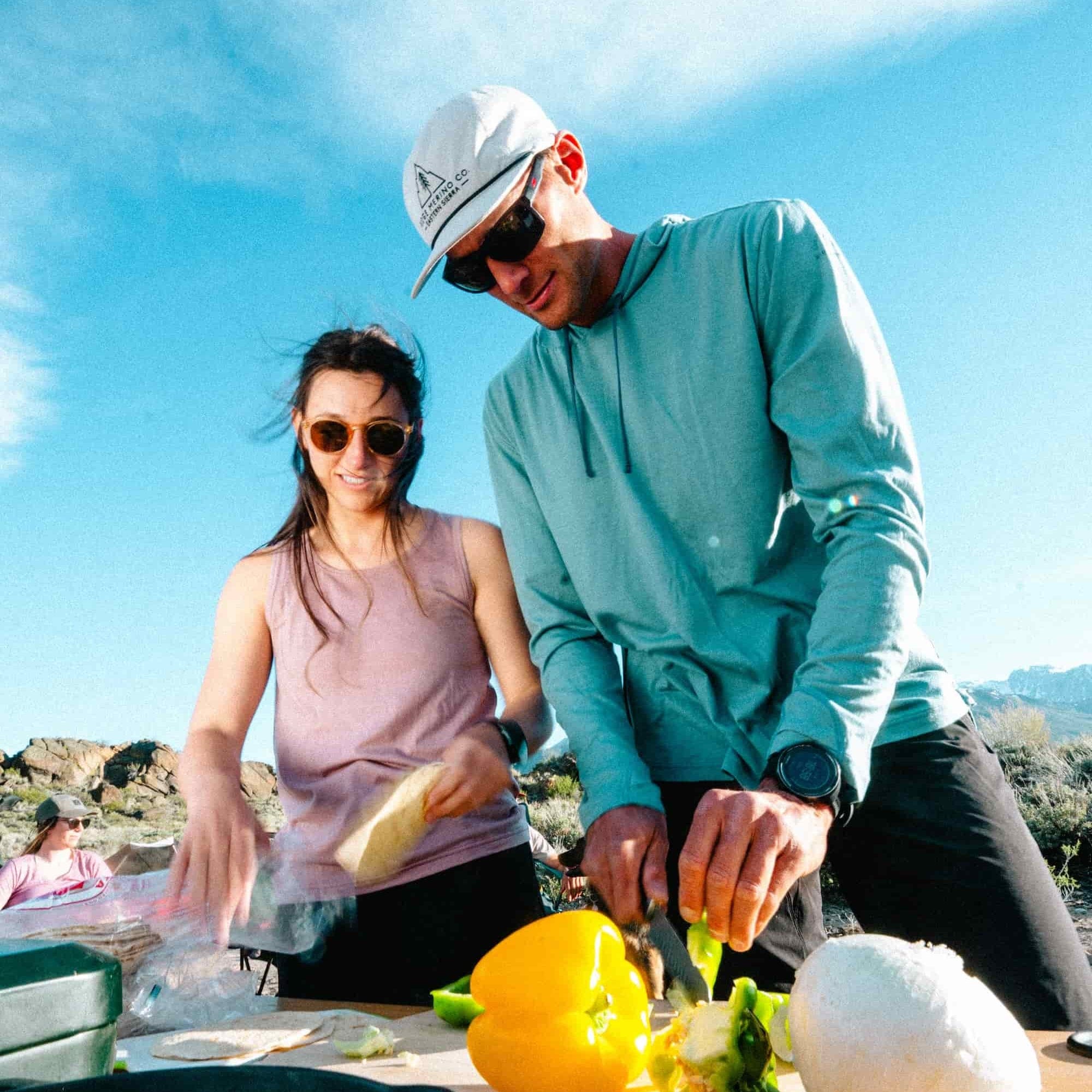 a man wearing a Ridge Merino Solstice Sun Hoodie cooking dinner while camping
