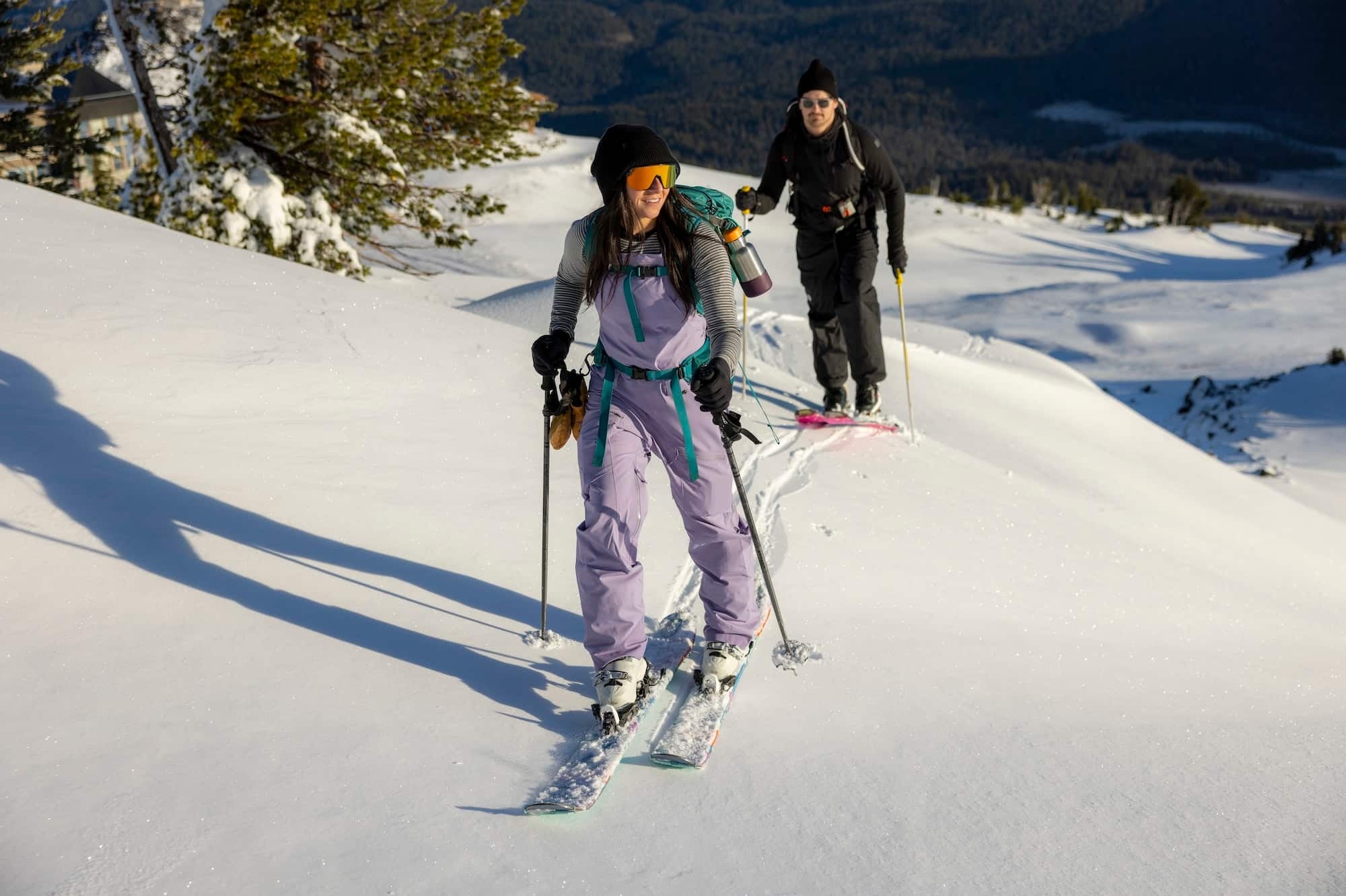 two backcountry skiers smile skinning up a snowy hill