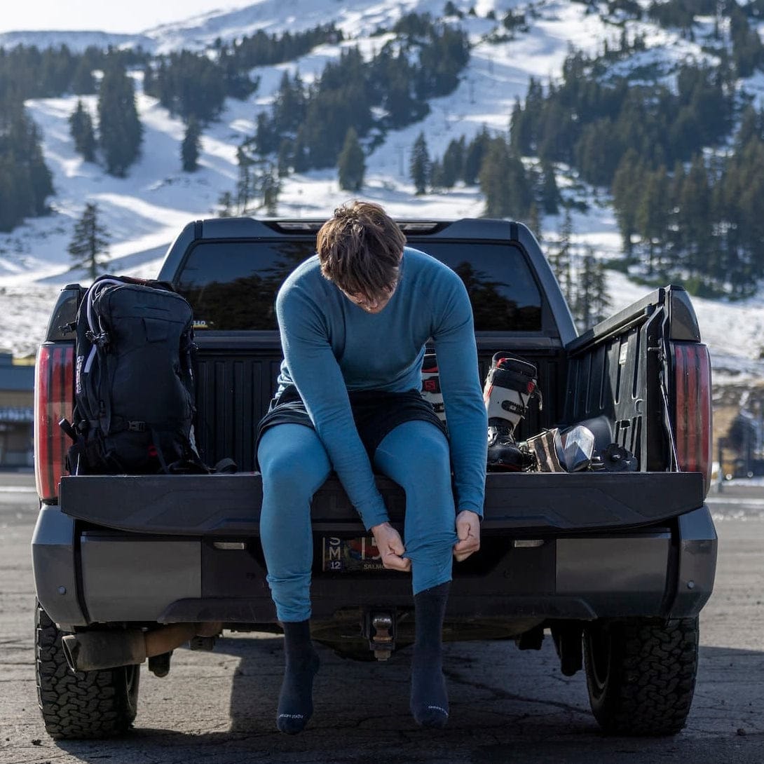 a man putting on ski socks wearing Ridge base layers and Hyde Merino Shorts over his base layers for extra warmth