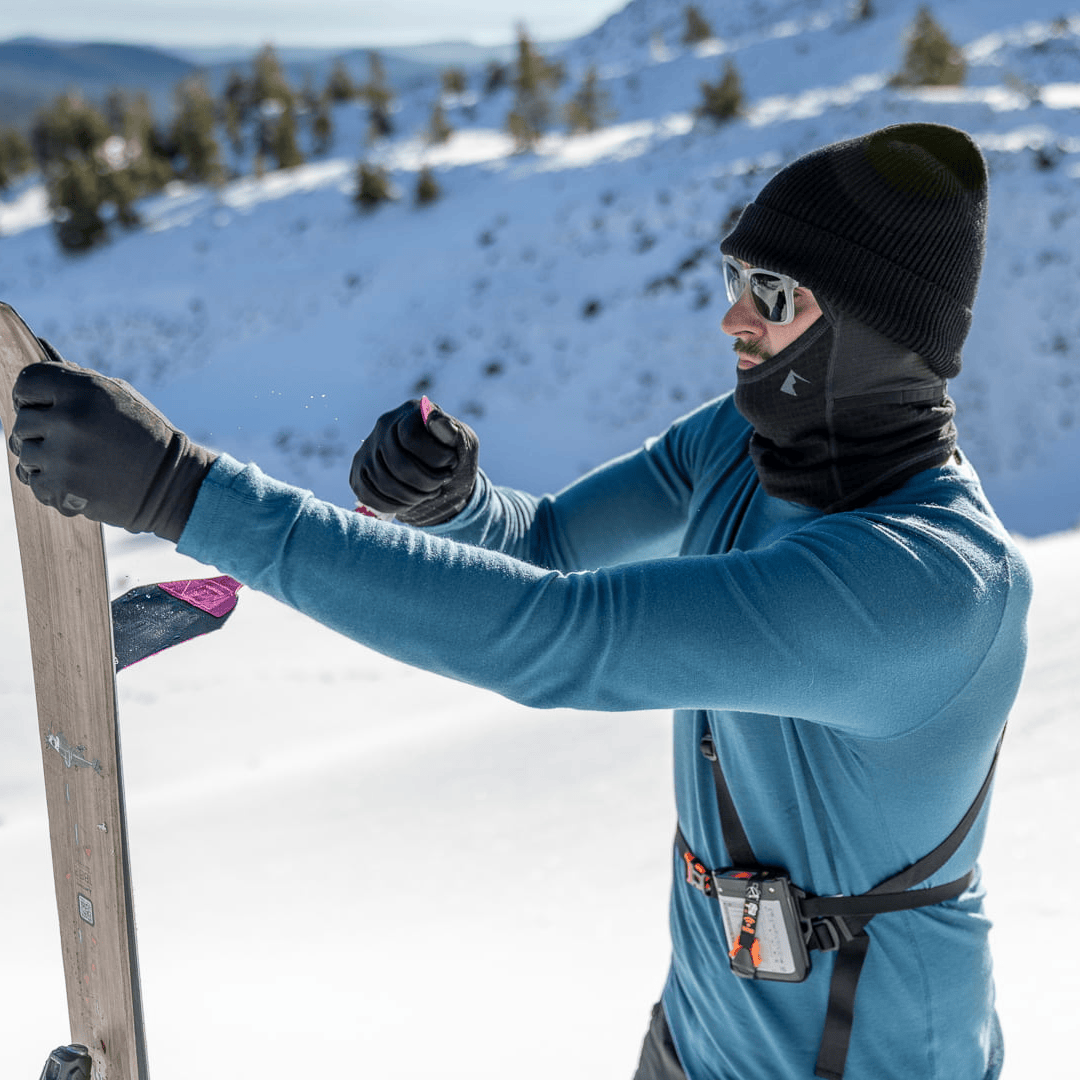 a man putting skins on his skis wearing an Inversion base layer shirt with a Cloudripper Balaclava, Ridge Beanie and Northwind Fleece Gloves