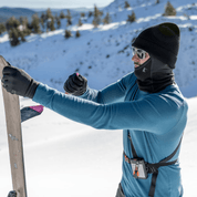 a man putting skins on his skis wearing an Inversion base layer shirt with a Cloudripper Balaclava, Ridge Beanie and Northwind Fleece Gloves