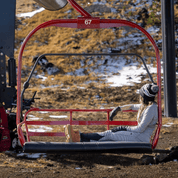 a woman sitting on a chairlift in early winter wearing Ridge Merino Inversion 100% Merino Base Layers and a Ridge beanie