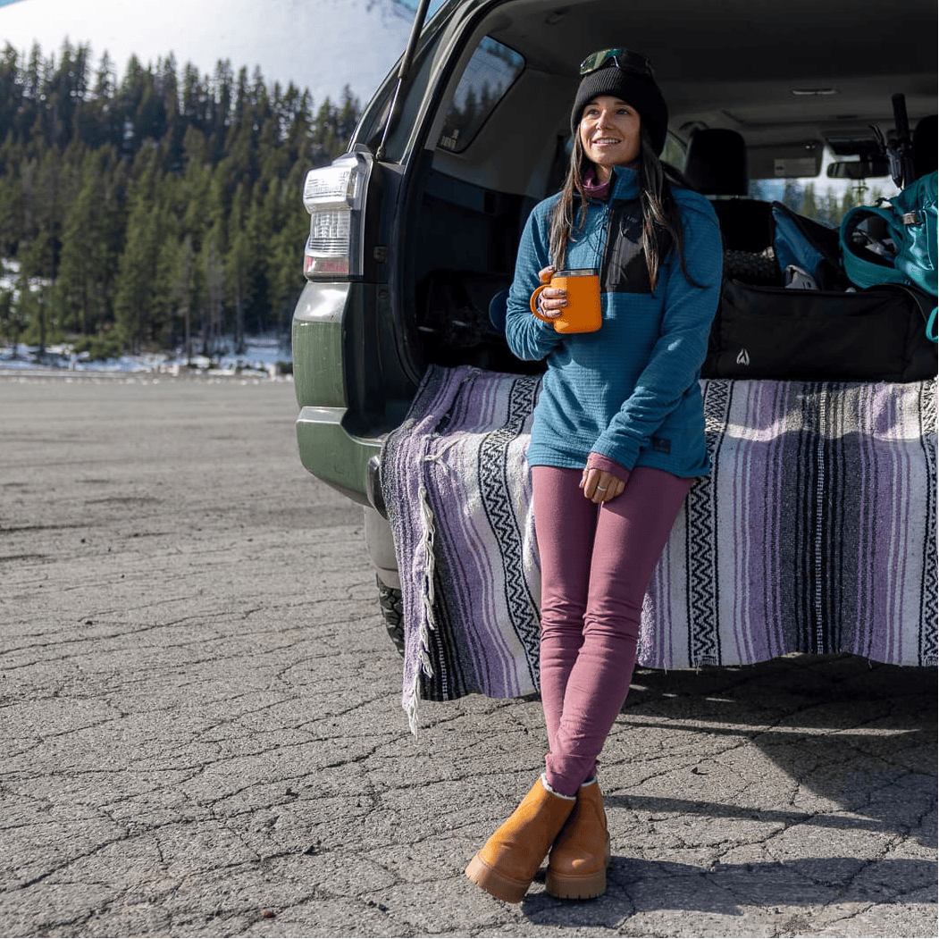 a woman getting ready for a ski day at her car wearing Aspect High Rise Bottoms and a blue Cloudripper Half Zip Pullover