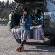 a woman getting ready for a ski day sitting on her car's tailgate