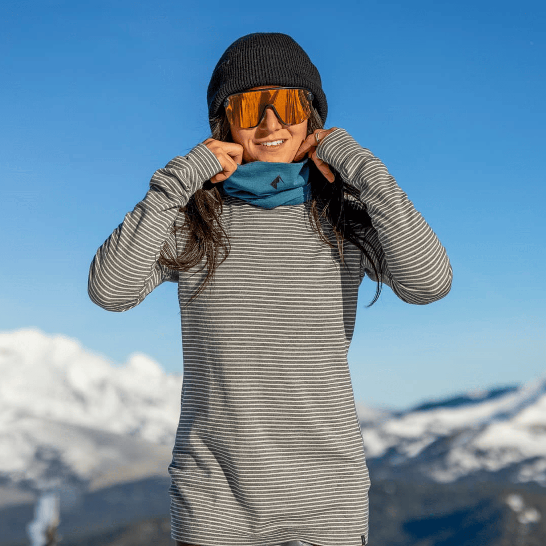 a woman layering up for a ski day wearing Ridge Inversion Base Layers and a blue neck gaiter and black beanie