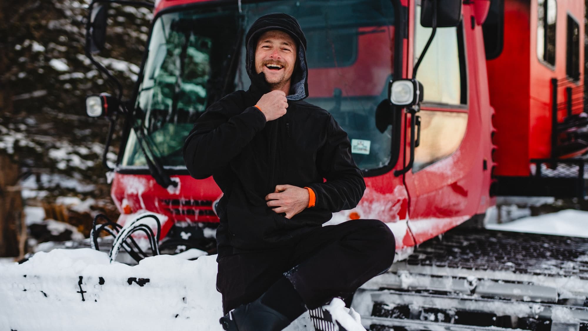 a man laughs wearing an Alpha Merino Wool Insulated Jacket in front of a snowcat