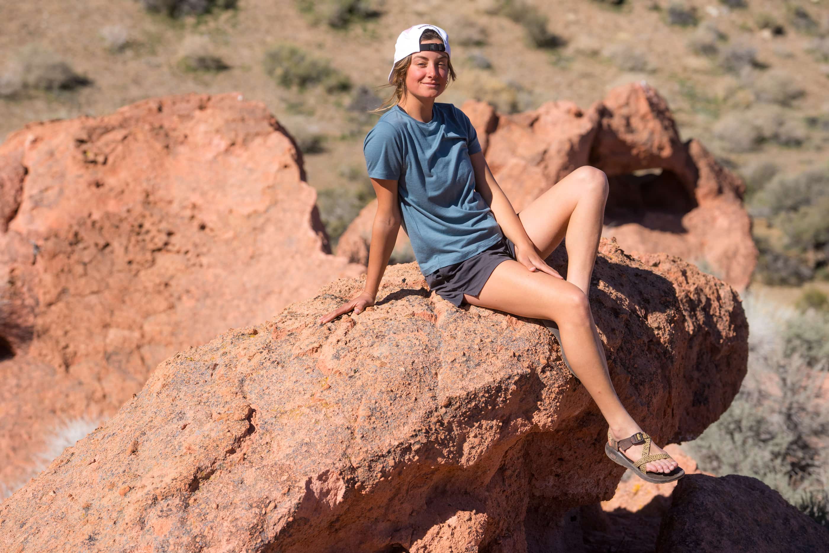 a woman sitting on a rock wearing a blue Journey Merino Wool T-Shirt