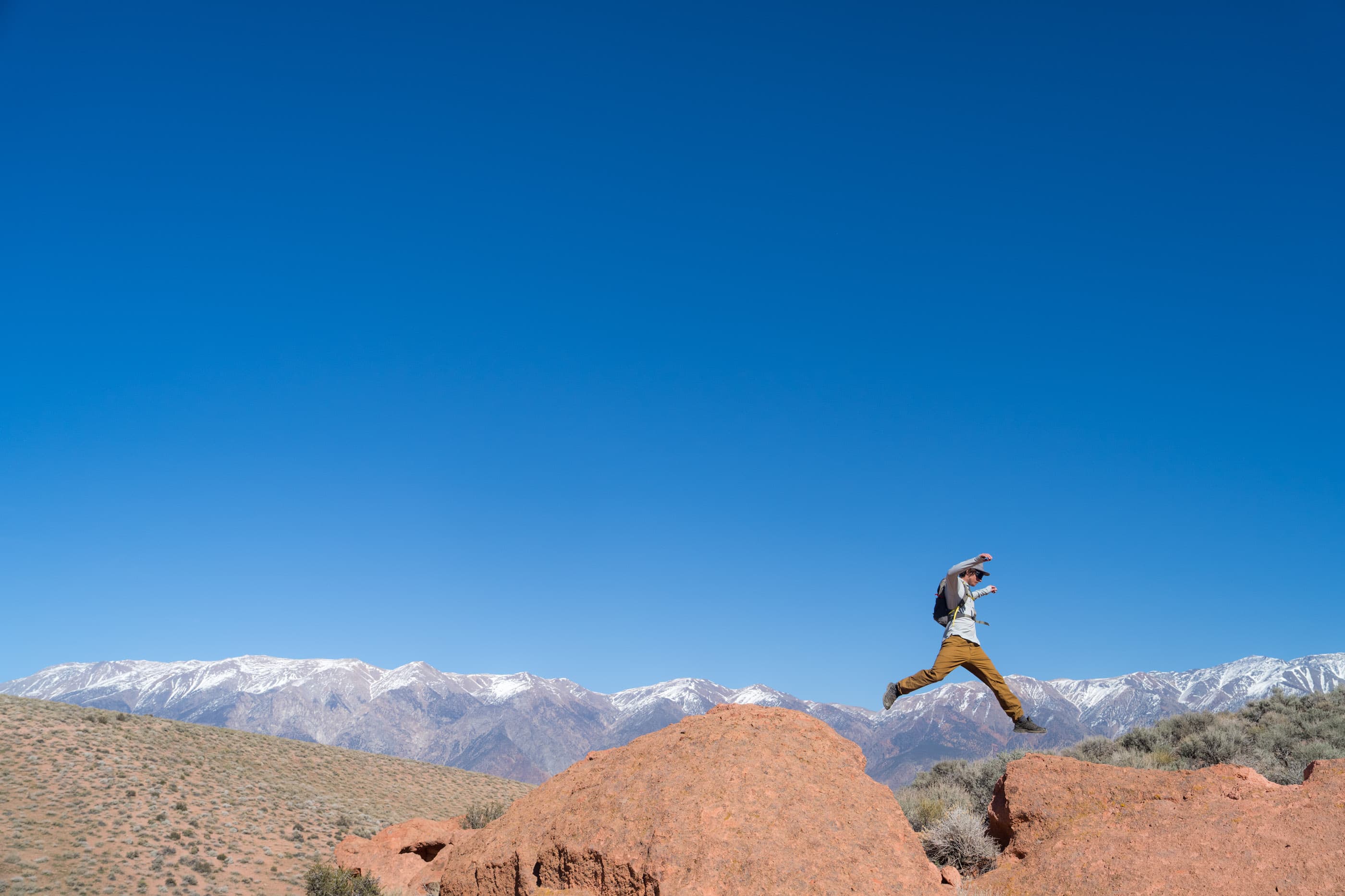 a man jumping from one rock to another in a Solstice Pro Sun Hoodie