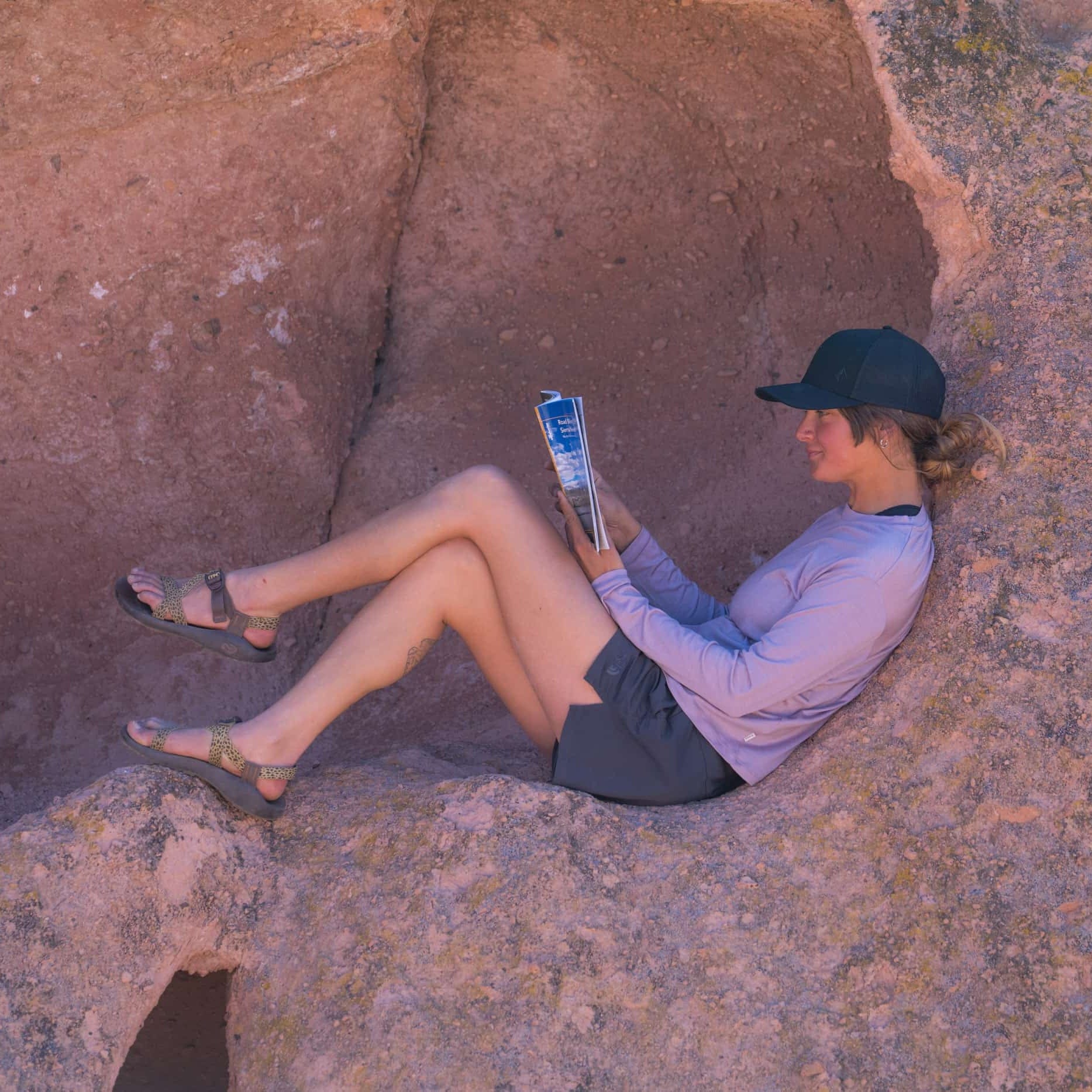 a woman reading a book in a rock nook wearing a pink long sleeve Merino Tencel shirt