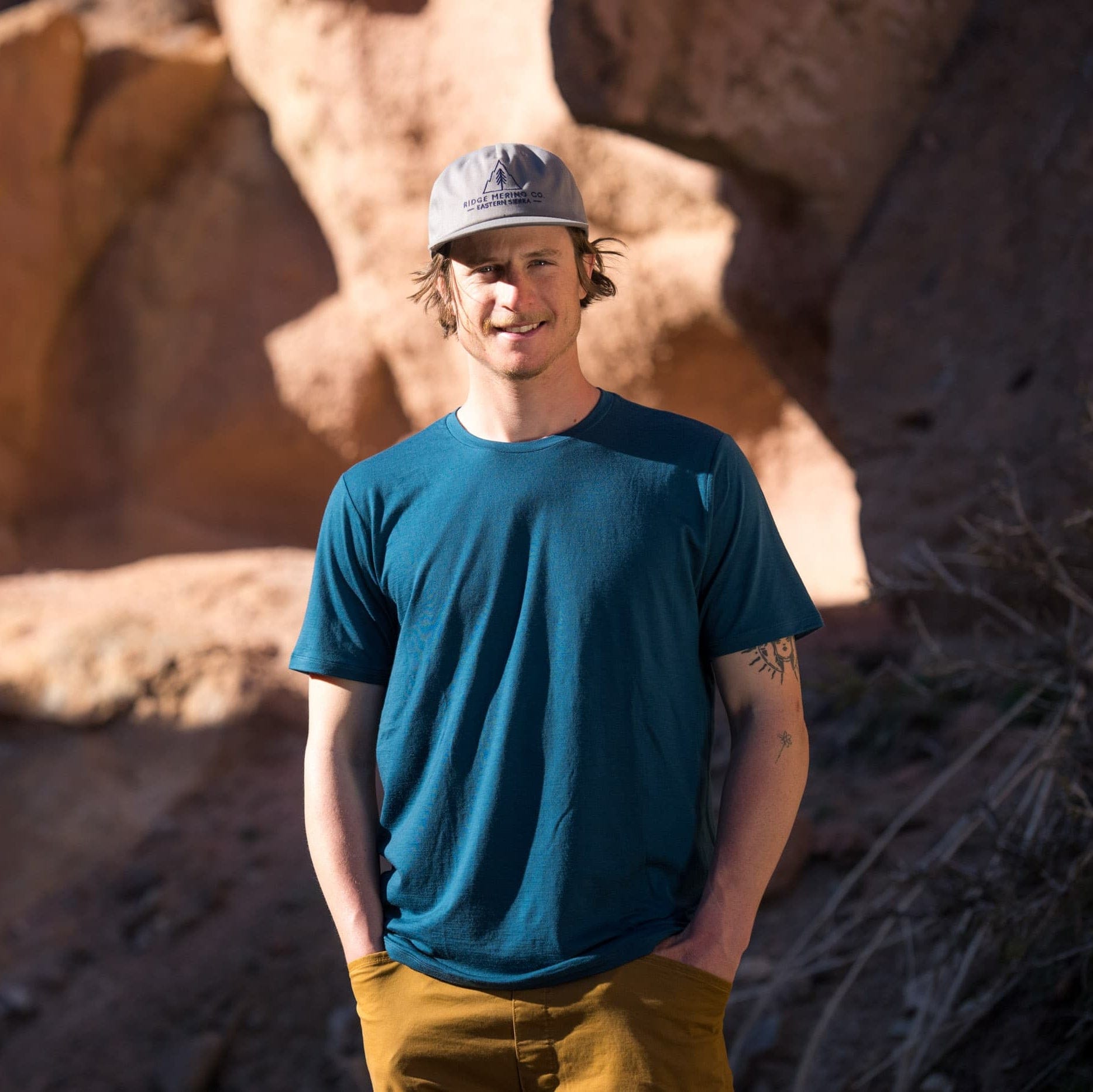 a man stands in a rocky area wearing a Journey Merino Wool T-shirt in Deep Current