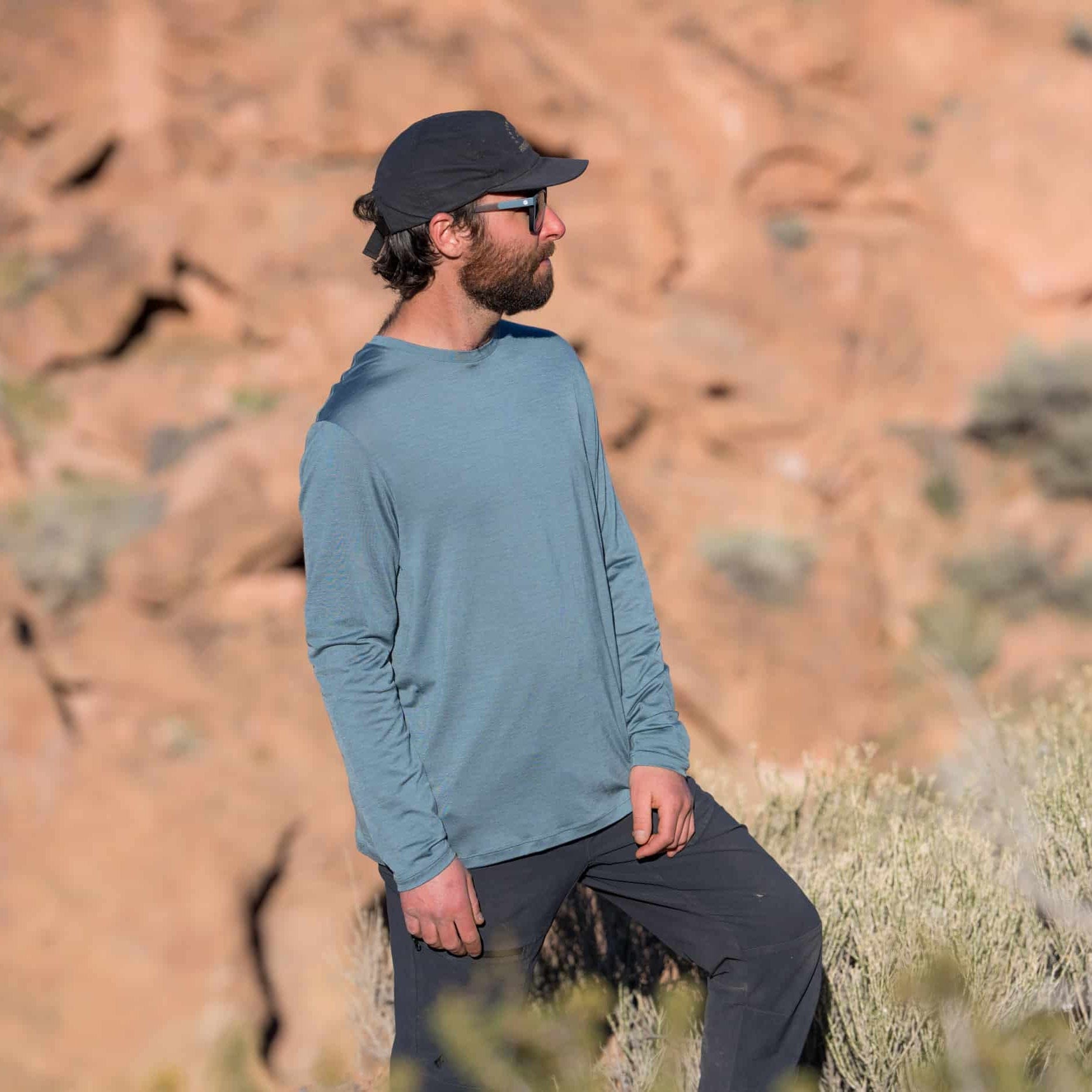 Man wearing a blue long-sleeve shirt and black cap in a desert landscape