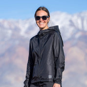 a woman in a black windbreaker standing on rocks on a mountain hike