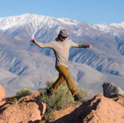 a man jumping from one rock to another wearing a Pursuit Air Ultralight Merino Hoodie