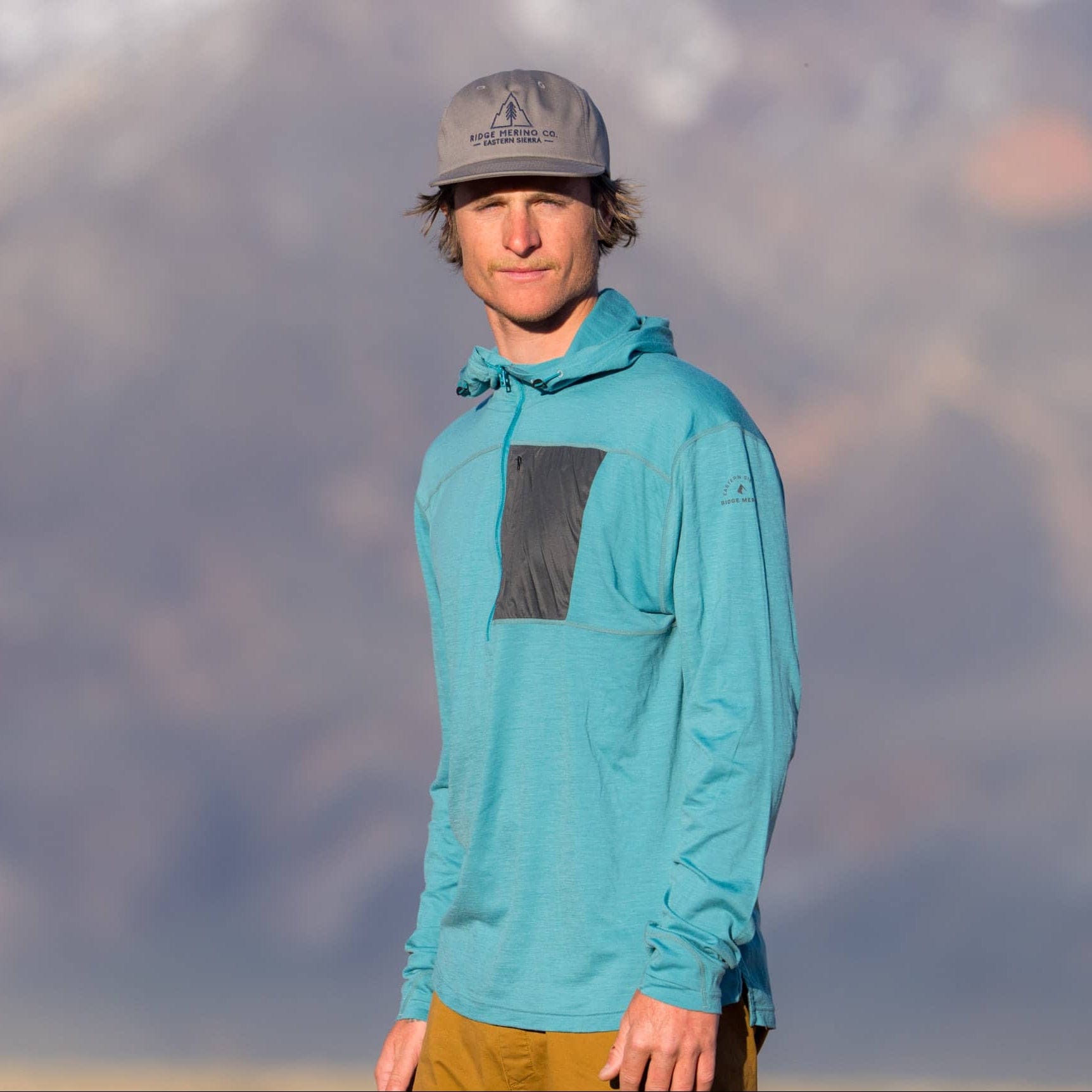a hiker wearing a teal Merino wool sun hoodie - the Solstice Pro Sun Hoodie with a quarter zip and gray chest pocket