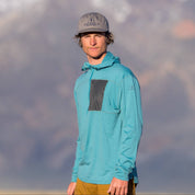 a hiker wearing a teal Merino wool sun hoodie - the Solstice Pro Sun Hoodie with a quarter zip and gray chest pocket