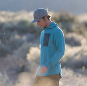 a hiker wearing a teal Merino wool sun hoodie - the Solstice Pro Sun Hoodie with a quarter zip and gray chest pocket