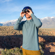 a man looking through binoculars wearing a Solstice Sun Hoodie in Overcast Blue