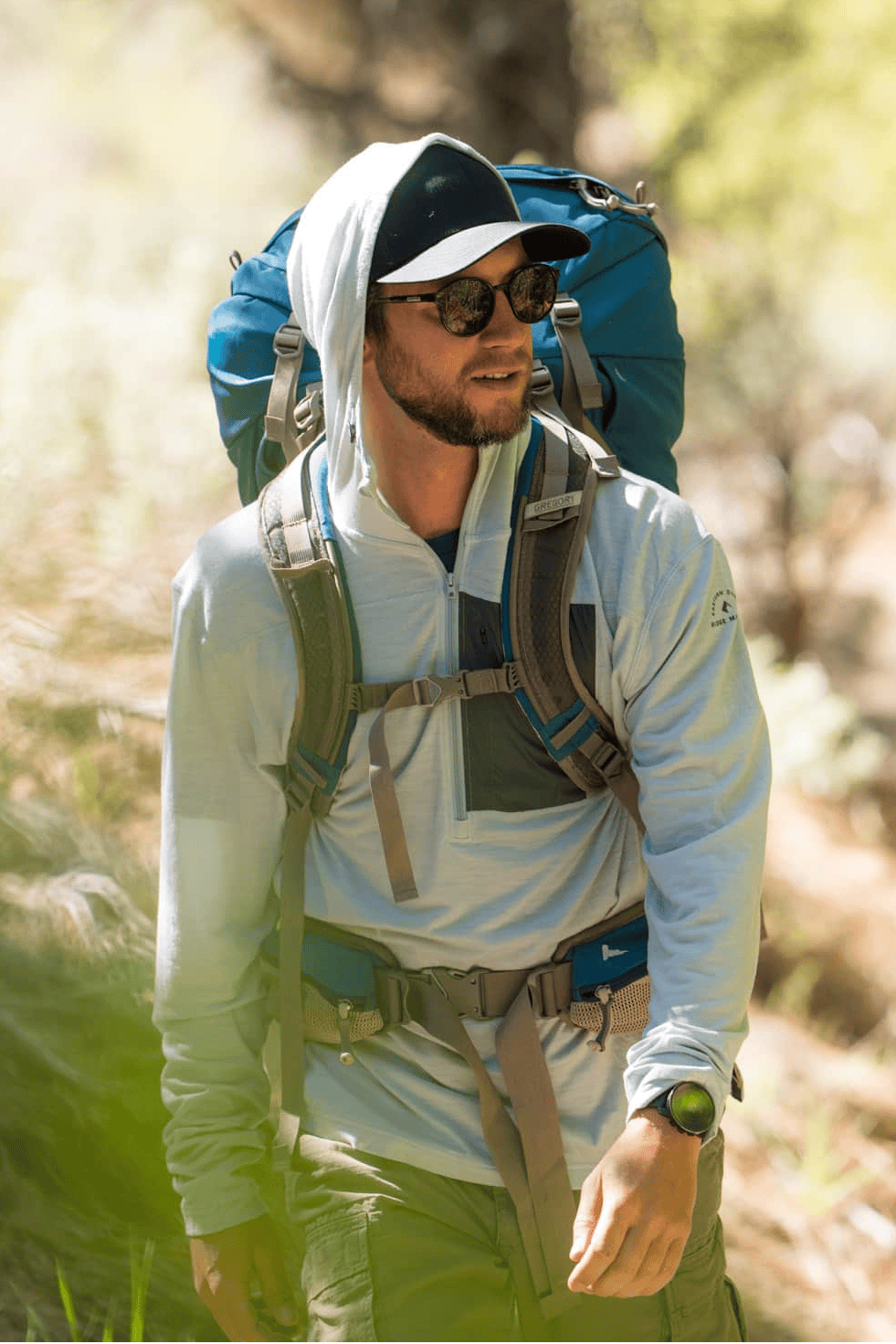 Man backpacking in a forest wearing a Solstice Sun Hoodie