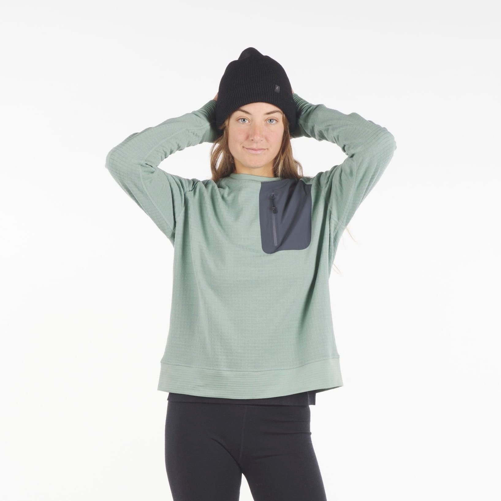 a woman wearing a Cloudripper Crew Neck Pullover in Iceberg Green with black Aspect base layer bottoms and a black Layton beanie