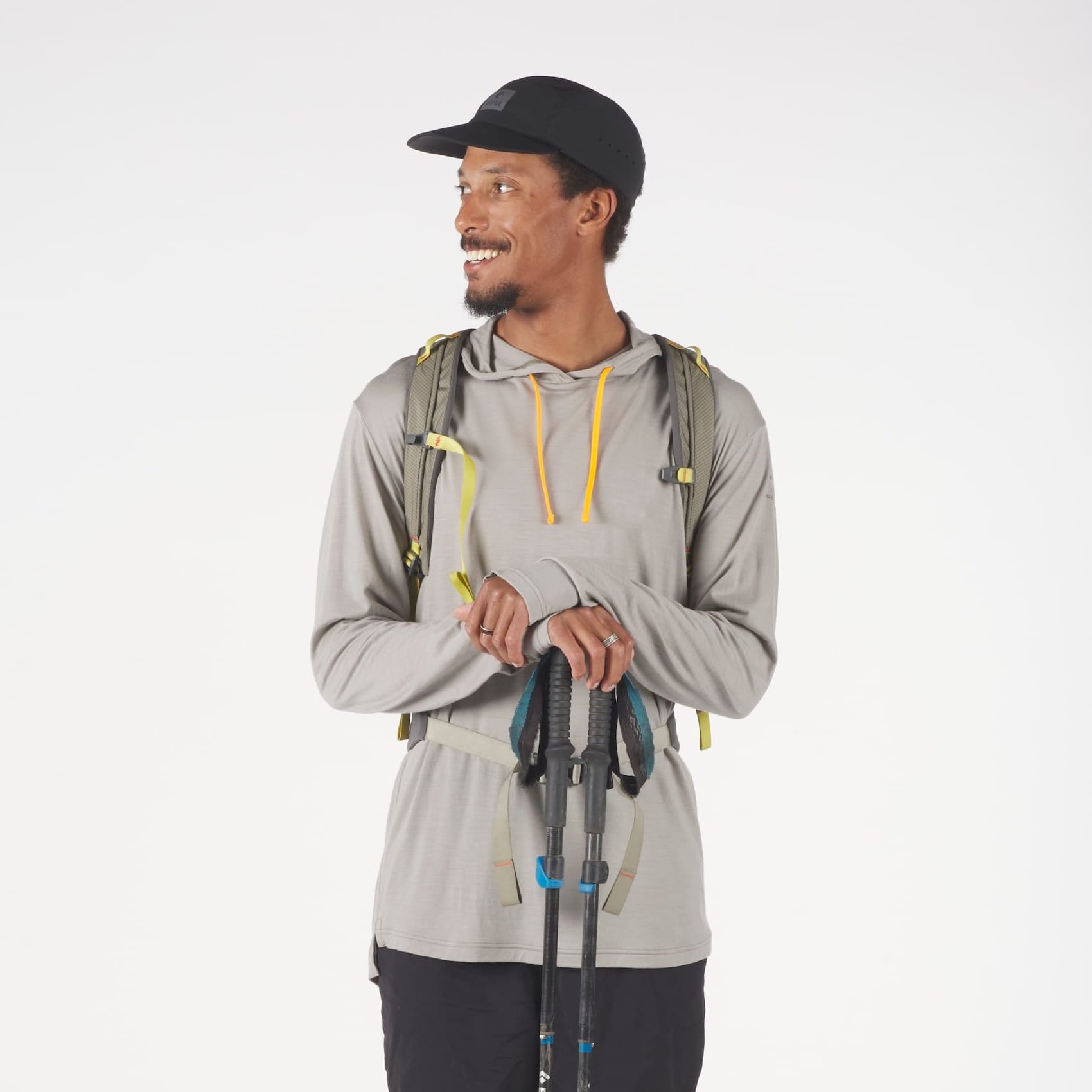 a man wearing a tan Solstice Merino Wool Sun Hoodie with a backpack, running hat and hiking poles