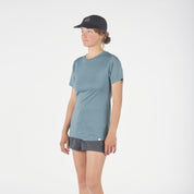 a woman wearing a blue Pursuit Ultralight Merino T-shirt, running shorts and a Ridge Run Hat