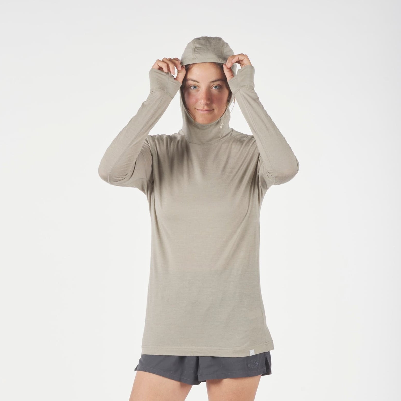 a woman adjusting the hood of her Pursuit Ultralight Merino Hoodie wearing running shorts