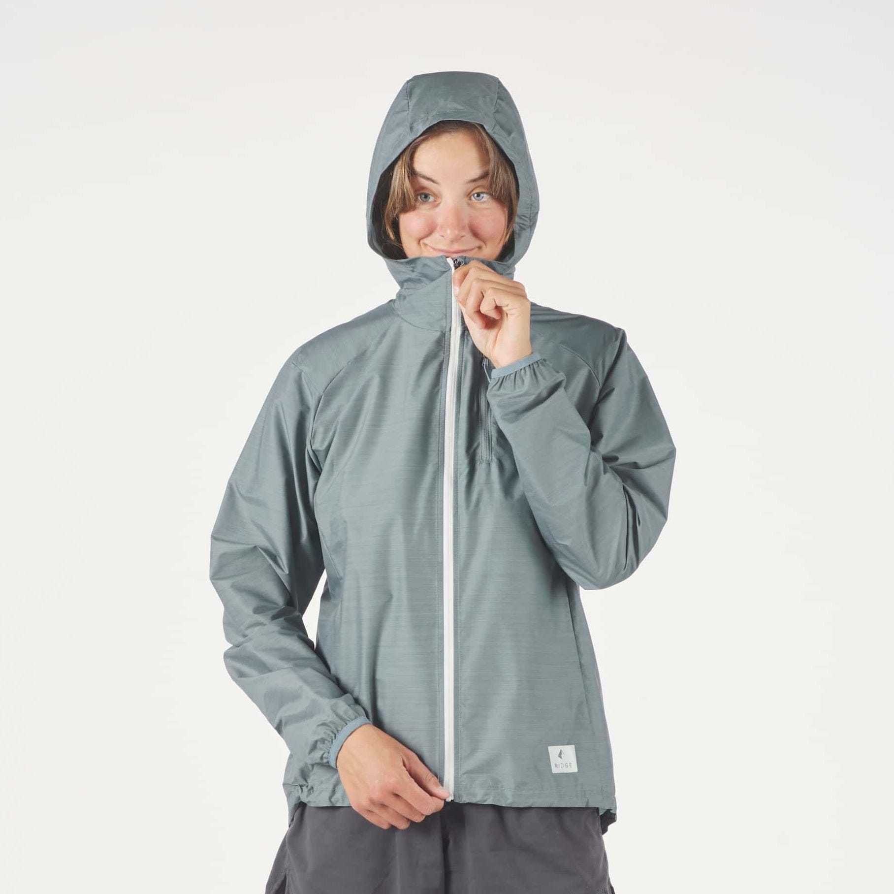 a woman zipping up her Windshifter Merino Windbreaker with the hood up