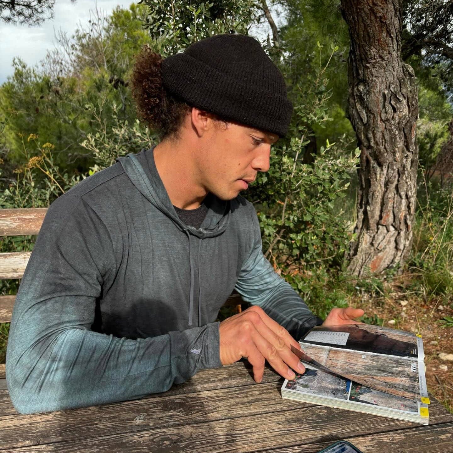 a man reads a climbing guide book wearing a Cement Dye Solstice Merino Sun Hoodie