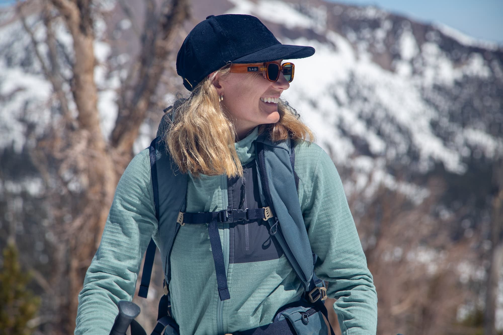 a skier smiles wearing a blue hat and Iceberg Green Cloudripper Full Zip Hoodie