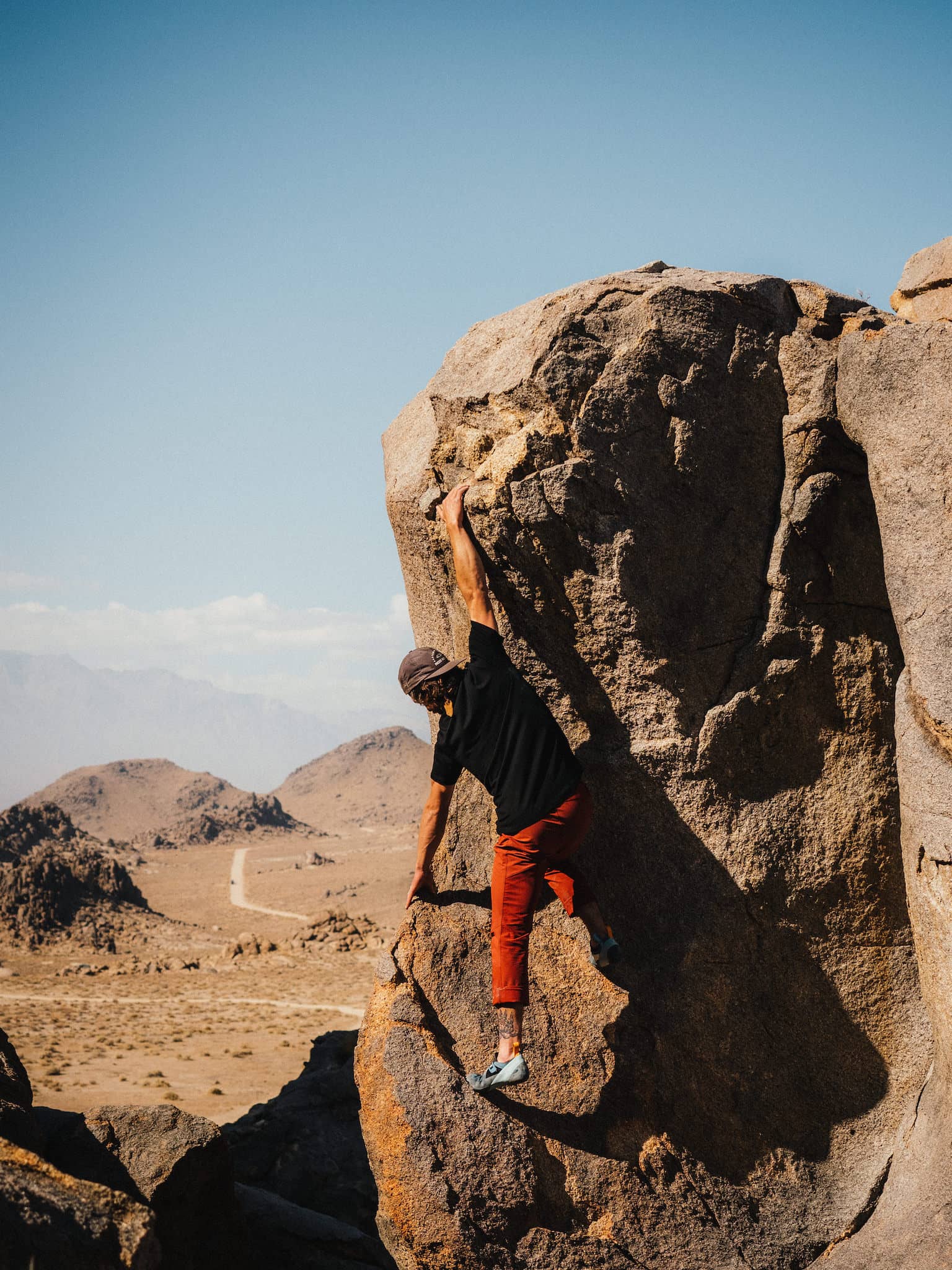 a man bouldering in a Ridge tee and bright orange pants