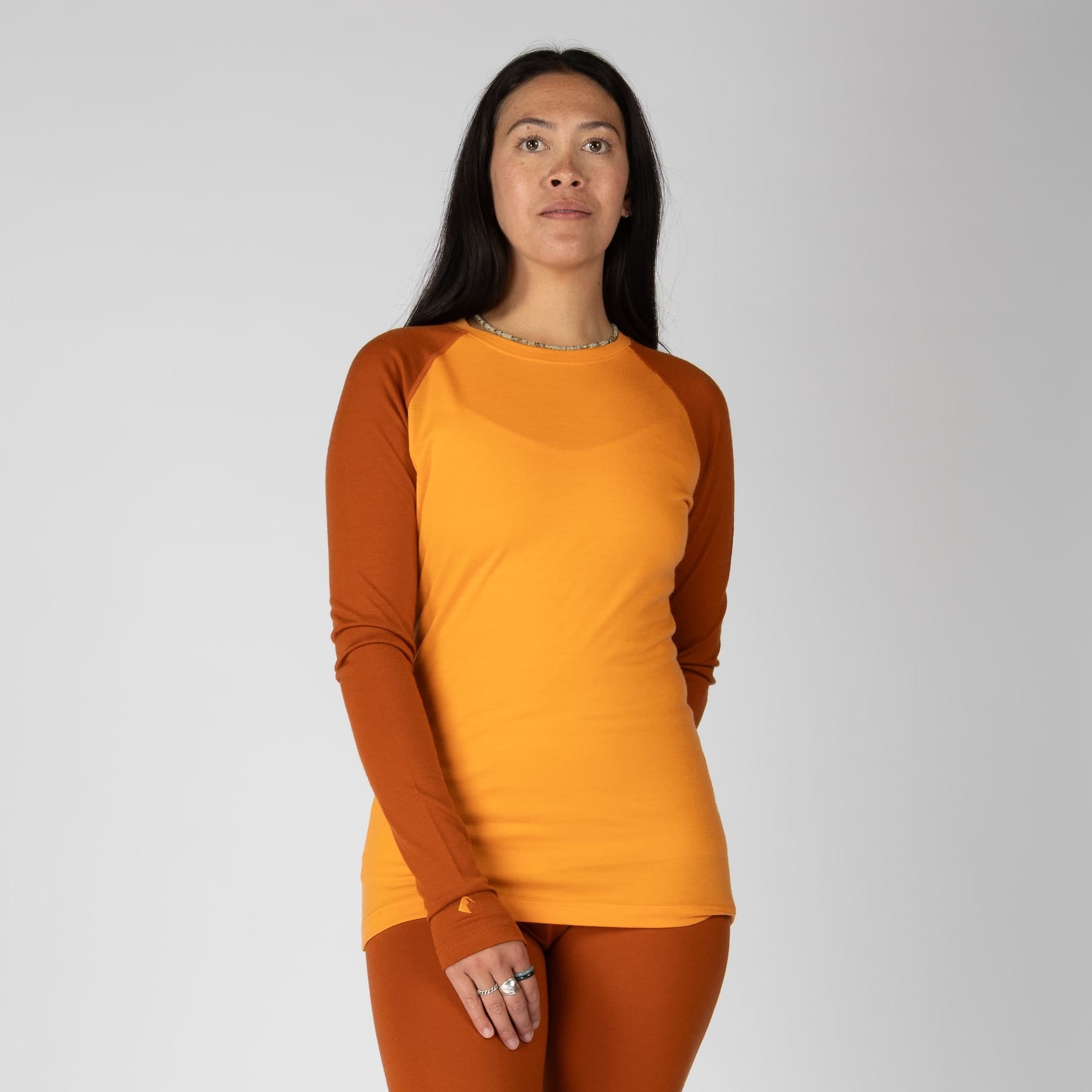 a woman wearing a Sun Orange and Cinnamon Aspect Base Layer Crew Top with matching bottoms