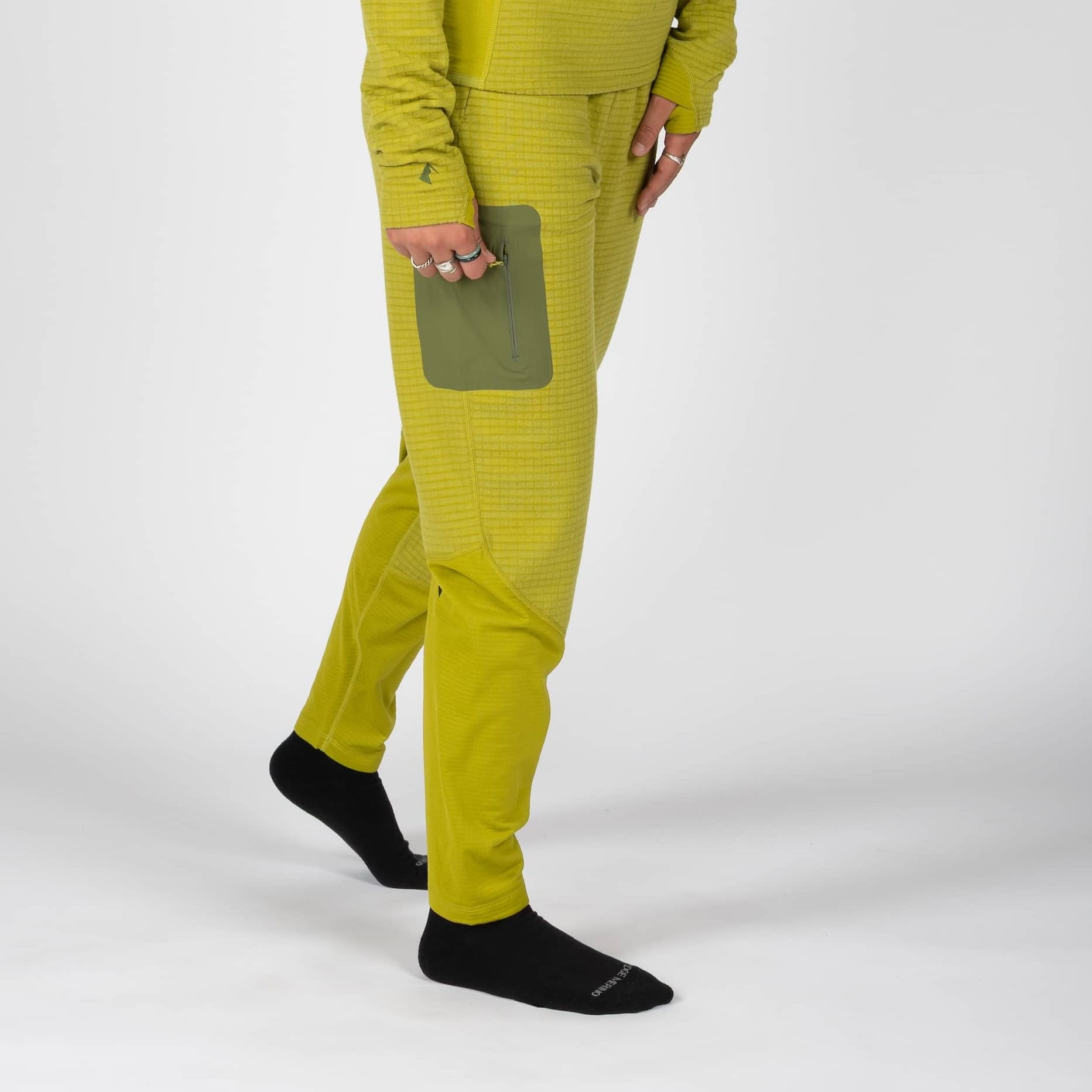 a woman zipping the side pocket on green Cloudripper Grid Fleece Pants
