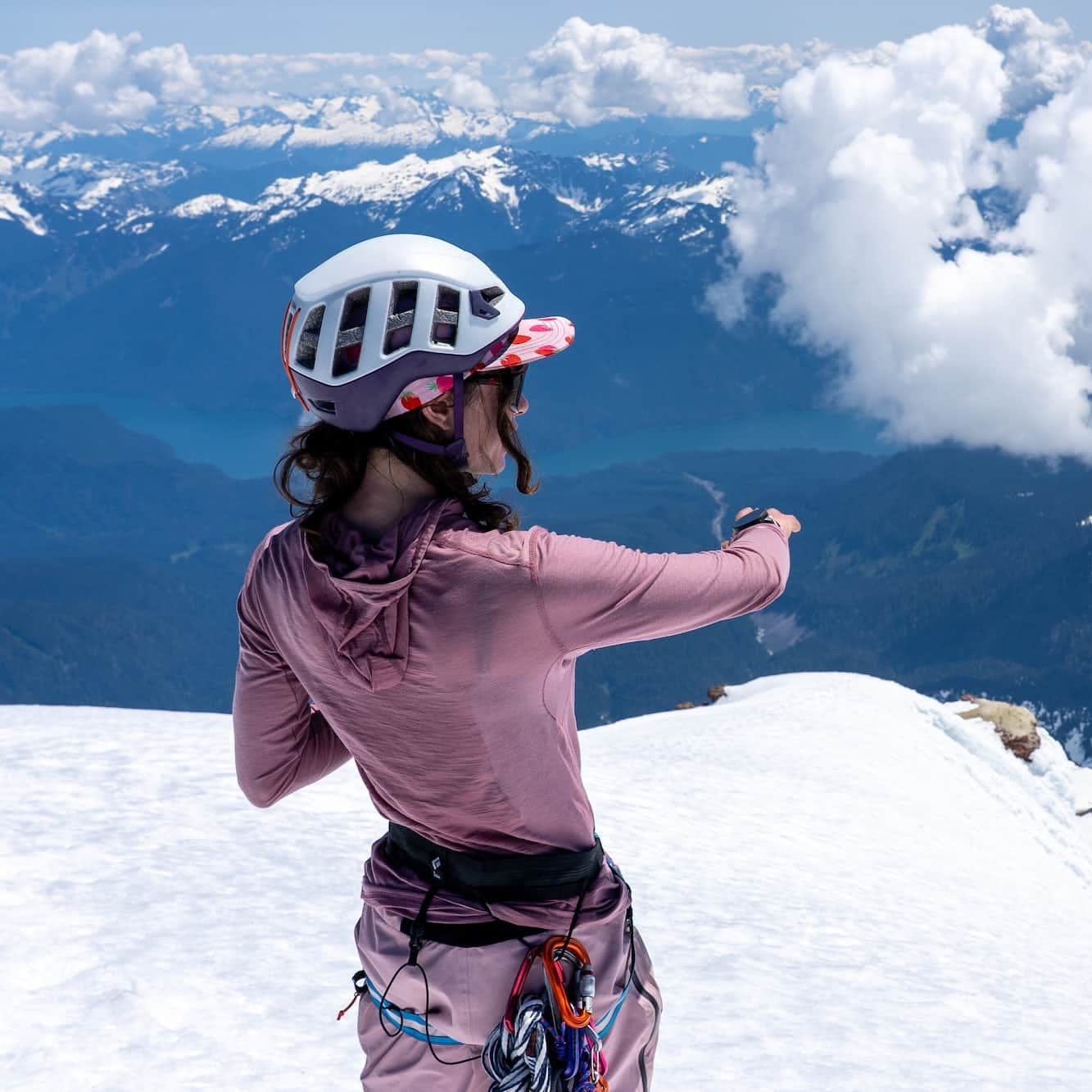a woman pointing down a mountain on a ski mission wearing an ultralight Pursuit Hoodie and helmet