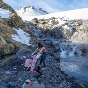 a woman gets undressed by a backcountry hot spring wearing Aspect Base Layer Bottoms and a pink Ridge Merino Bralette