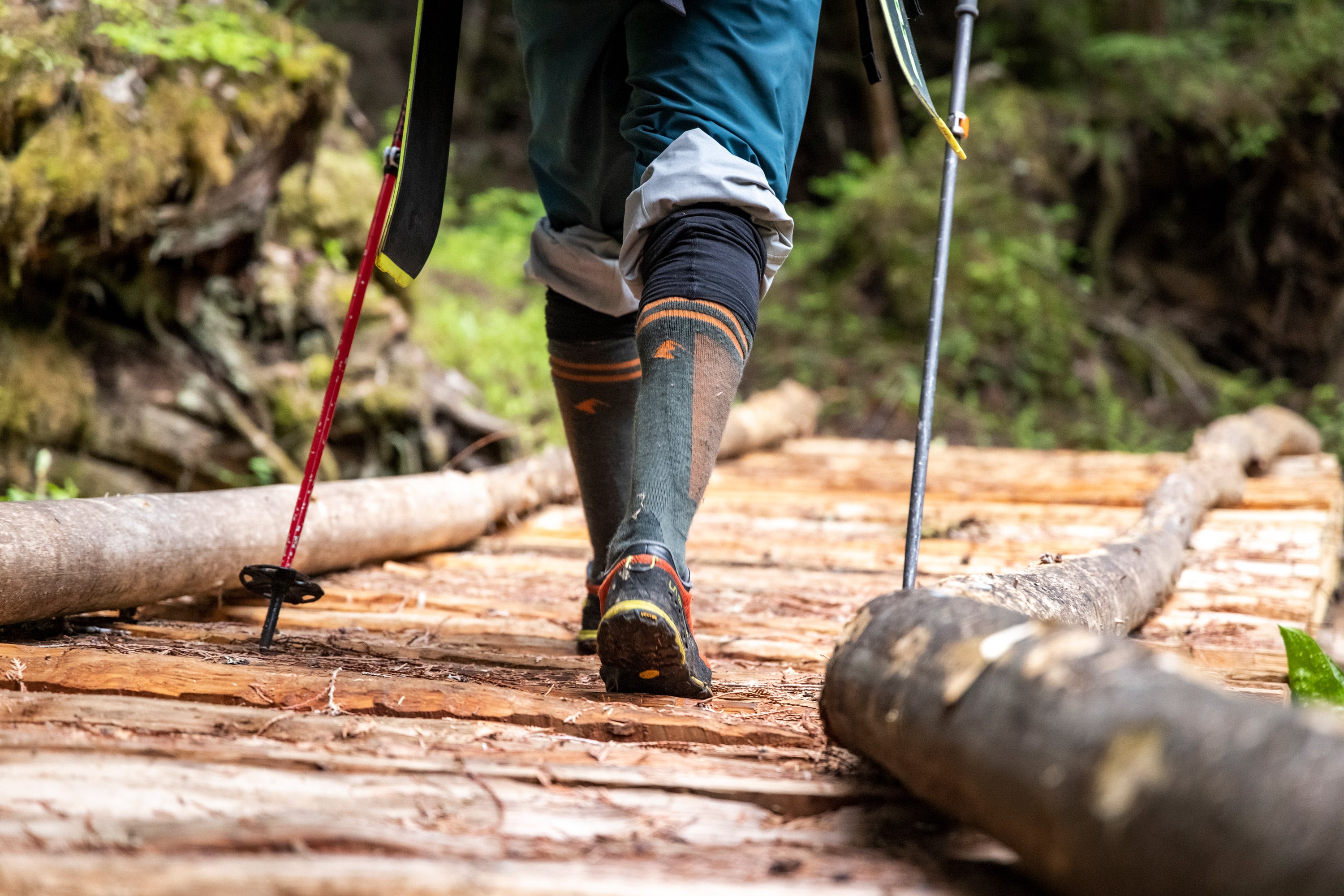 A person walks across a wooden bridge in tennis shoes and Ridge Merino socks heading out on a ski tour