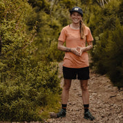 a woman wearing a Wander Crew Neck T-Shirt and Ridge Merino hat and socks smiles on a hiking trail