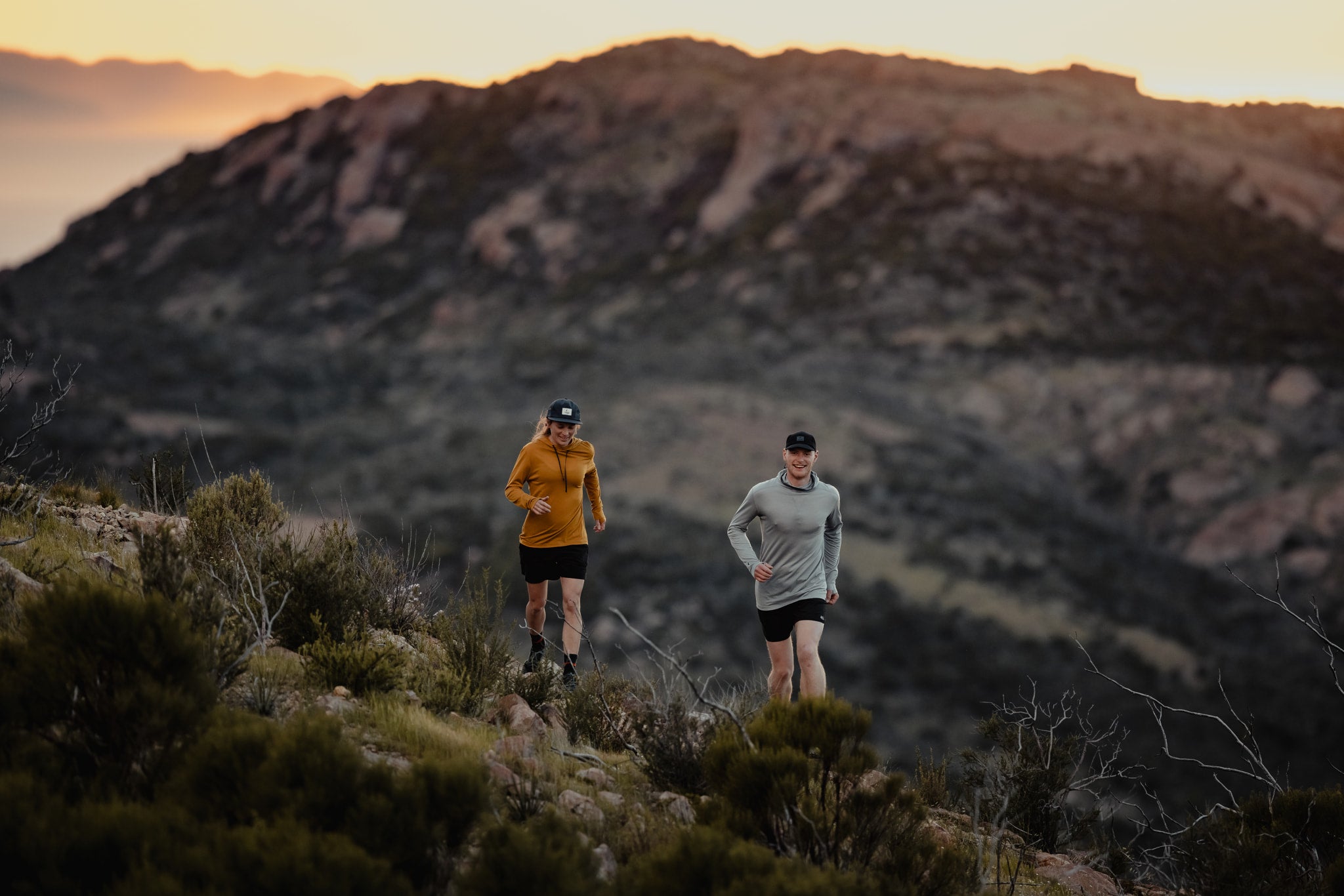 a man and a woman trail running wearing the Solstice lightweight merino wool hoodie and Pursuit lightweight hoodie