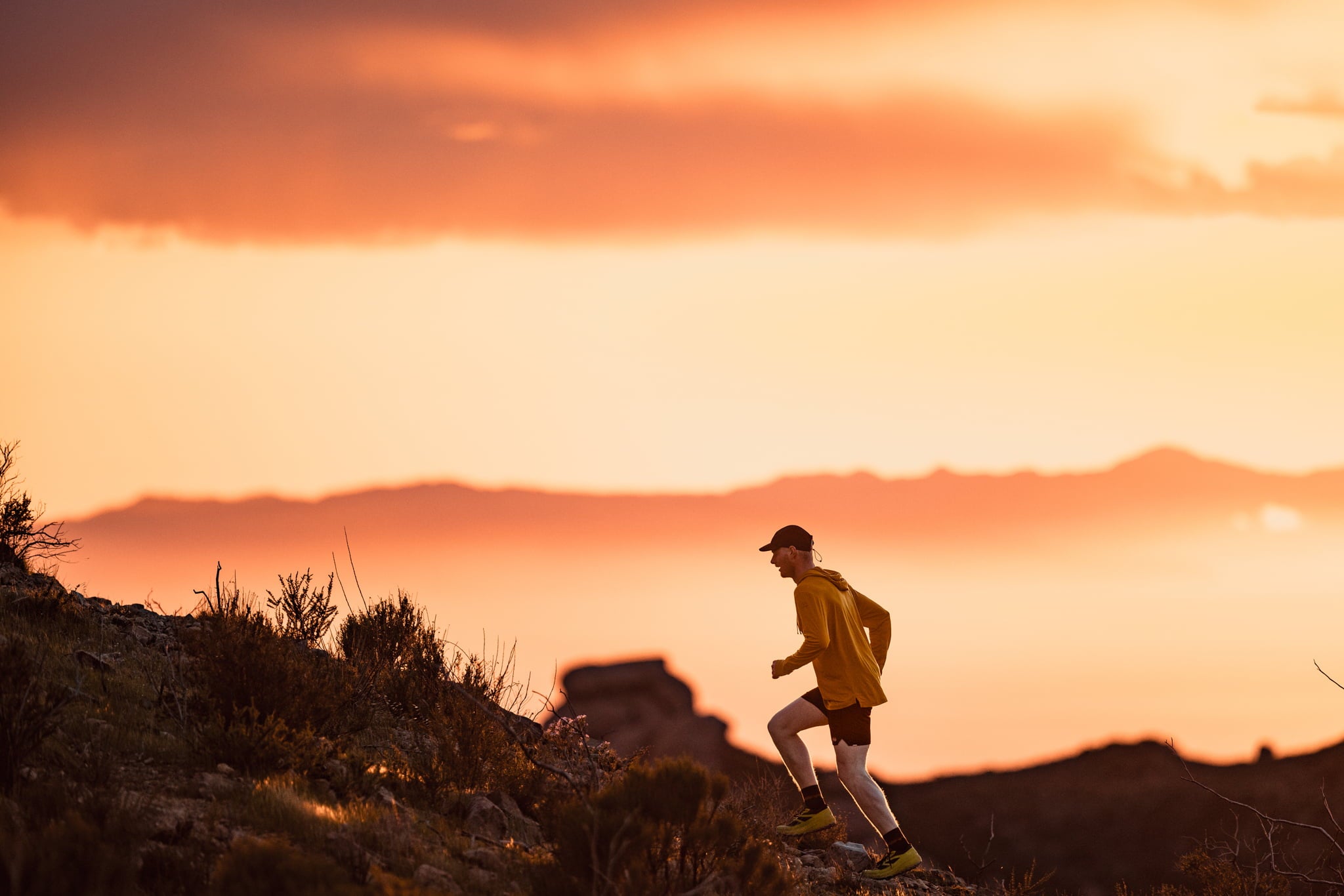 a trail runner running up a hill at sunset in a Solstice lightweight Merino wool hoodie