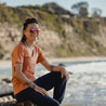 a woman wearing a Ridge Merino tee smiles sitting on a beach