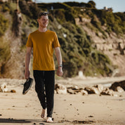 a man walking on a beach wearing the Goldenrod Journey Merino Wool T-Shirt