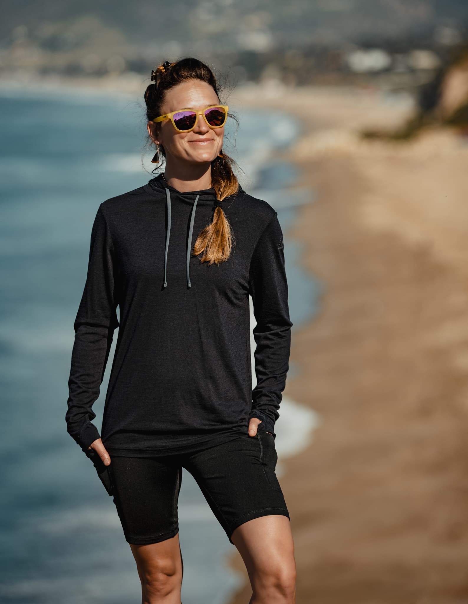 a woman on the beach wearing a Ridge Merino Sun Hoodie