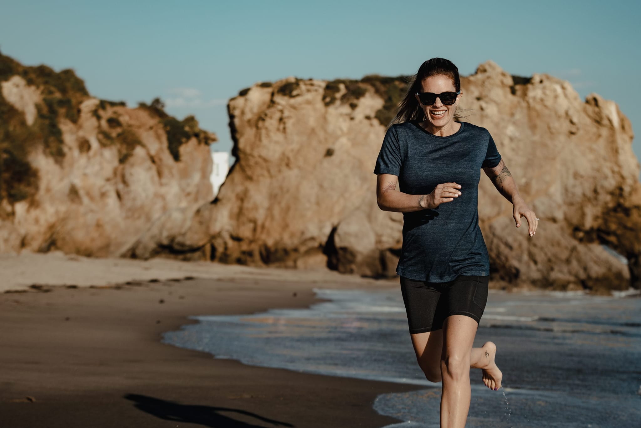 a woman laughs running on the beach wearing a Pursuit Tee