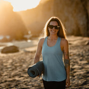 a woman holds a yoga mat on a beach wearing a Frankie Merino Wool Tank Top and sunglasses