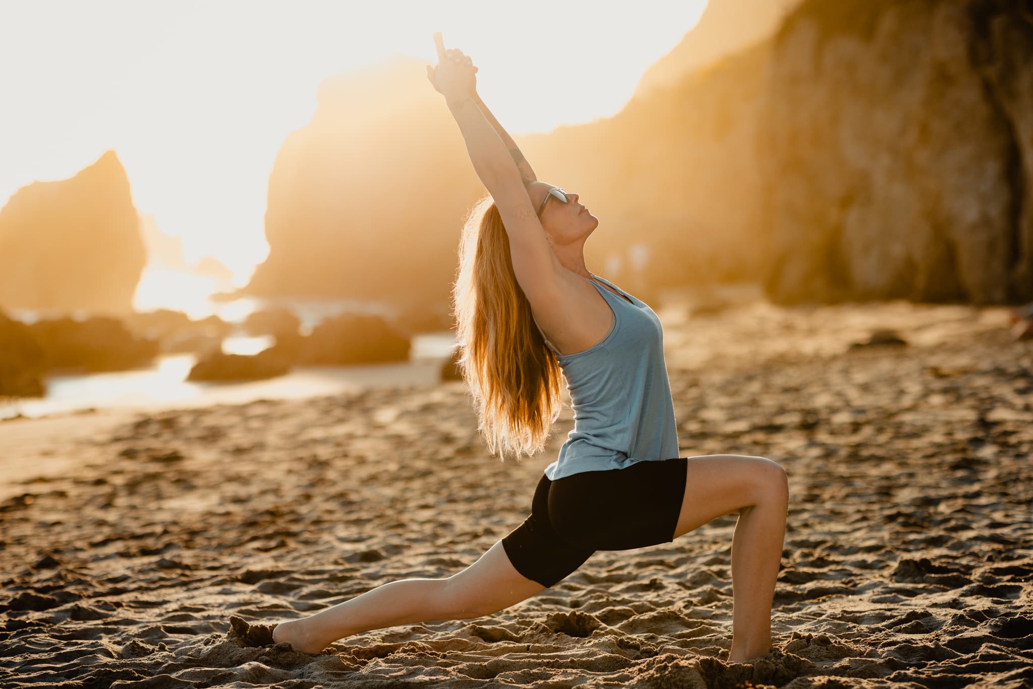 a woman does a yoga pose on the beach wearing Hilltop Bike Shorts and a Frankie Tank Top