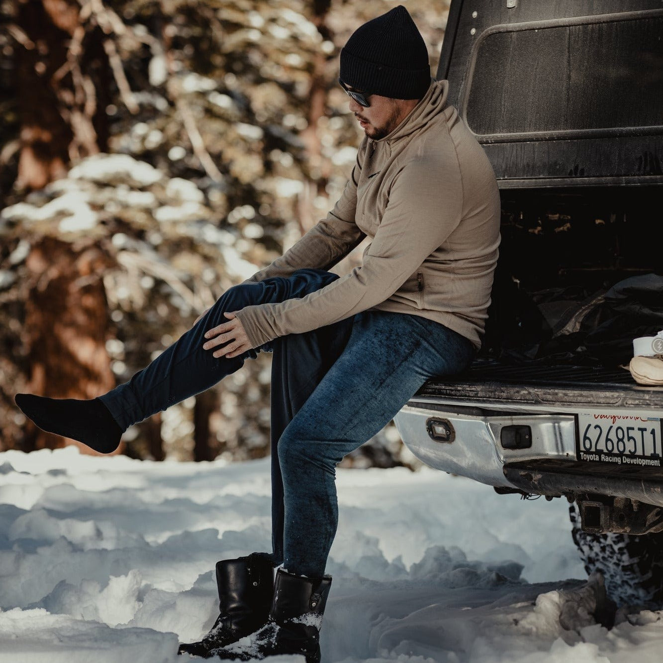 a man putting on Aspect Base Layer Bottoms for skiing wearing a Hyde Hoodie and Ridge beanie