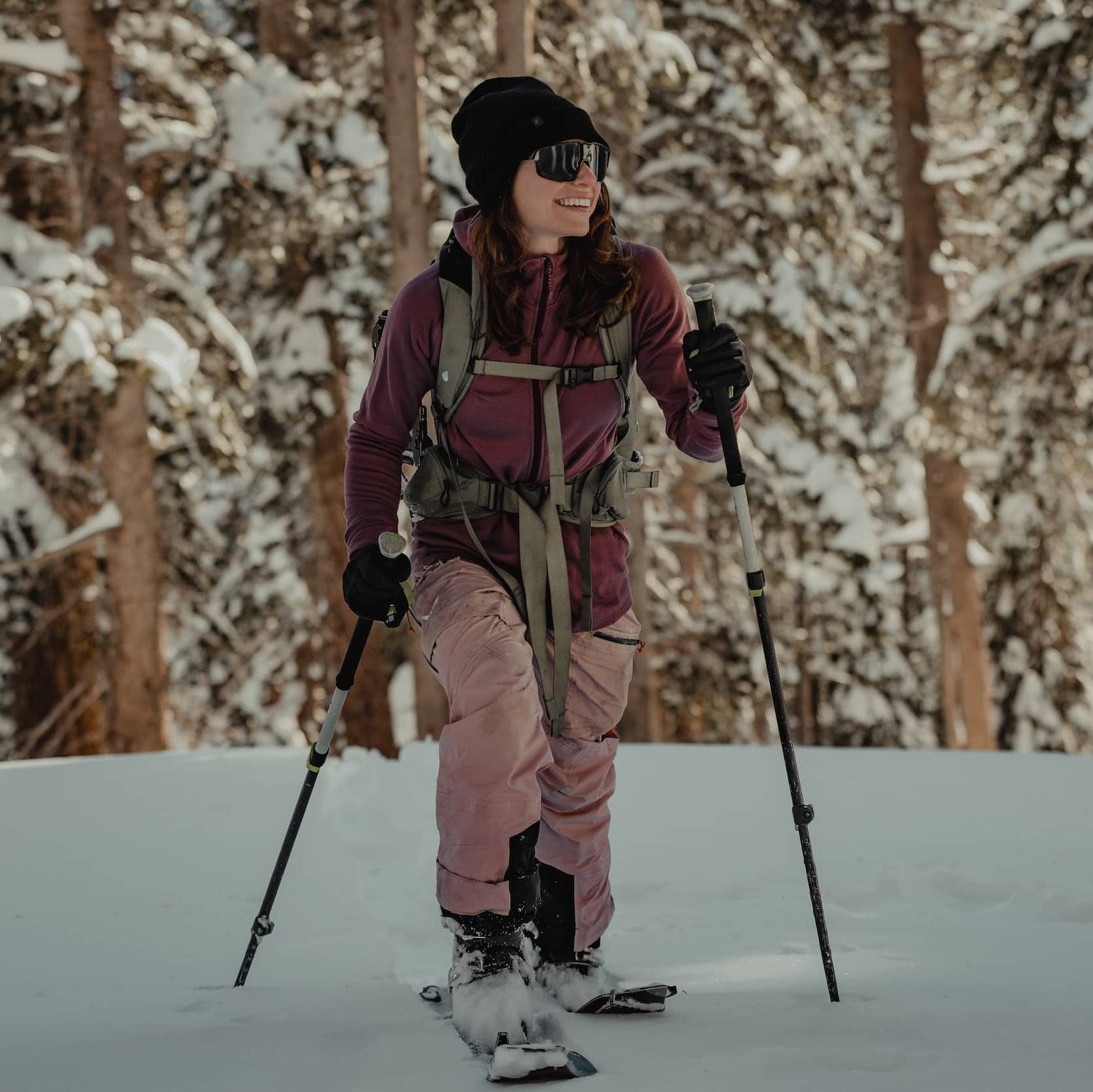 a woman smiles backcountry skiing in the woods