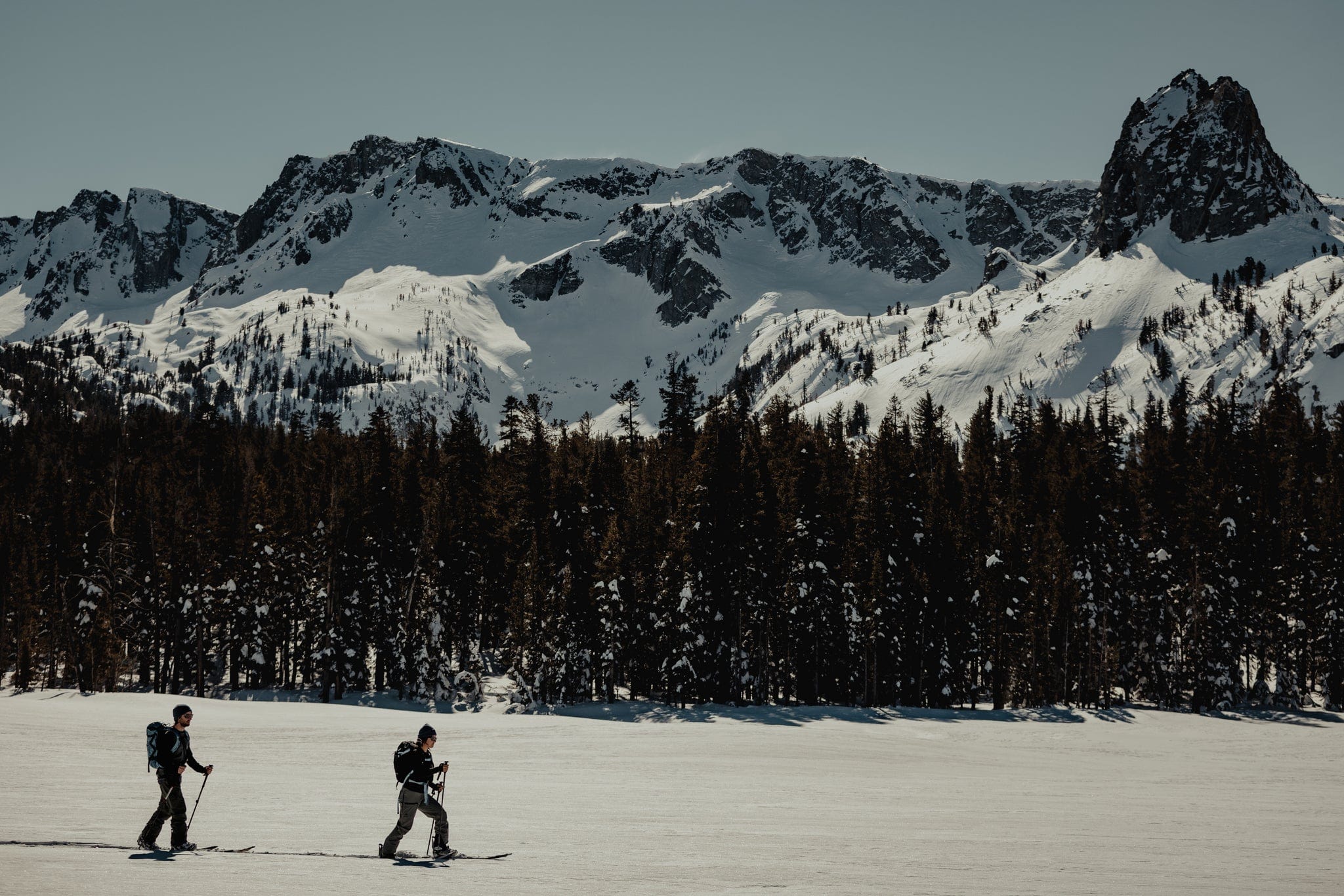 Two splitboarders skin across a frozen alpine lake in Mammoth Lakes, CA beneath Crystal Crag