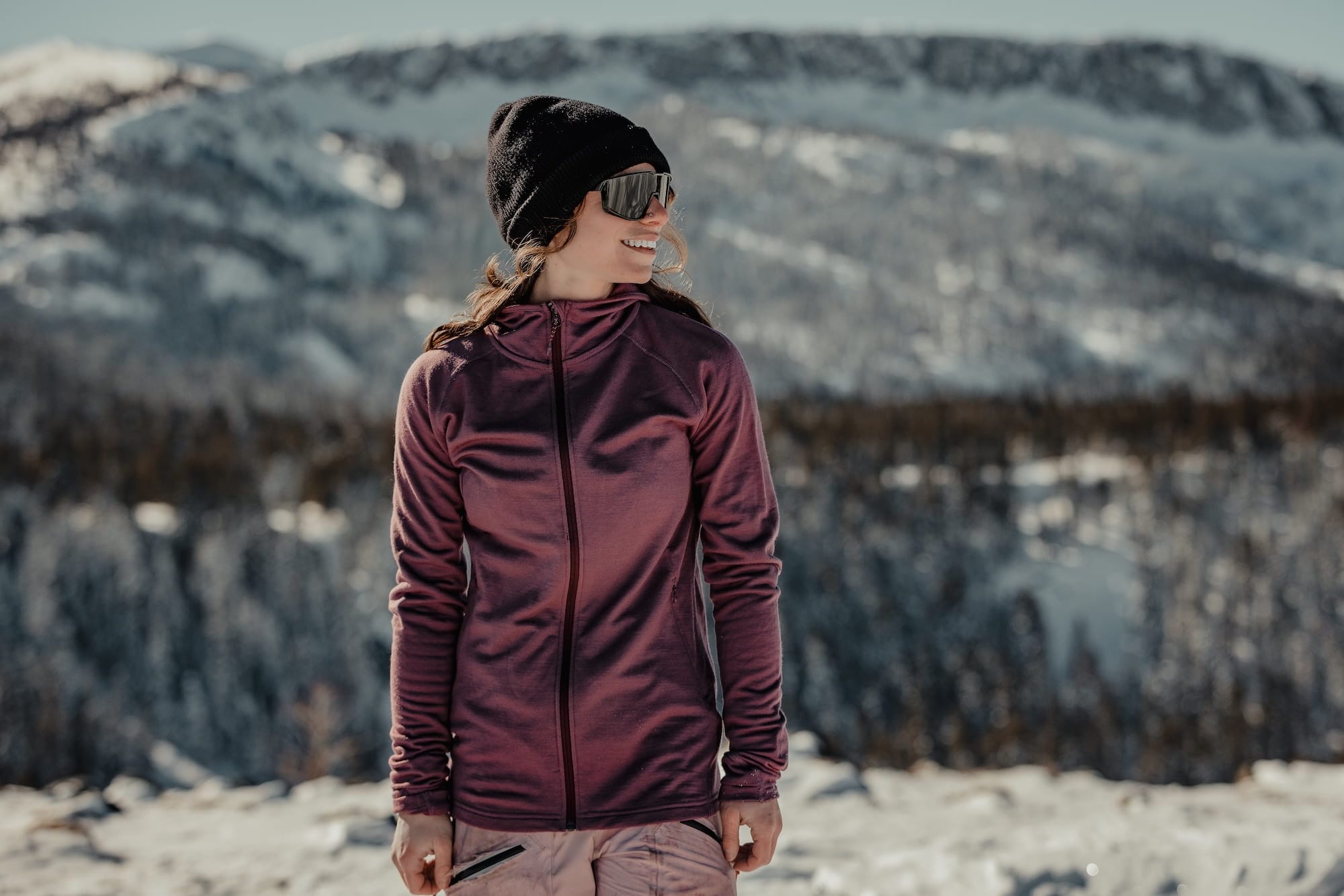 a woman smiles wearing a pink Hyde Hoodie in the snowy mountains near Mammoth Lakes