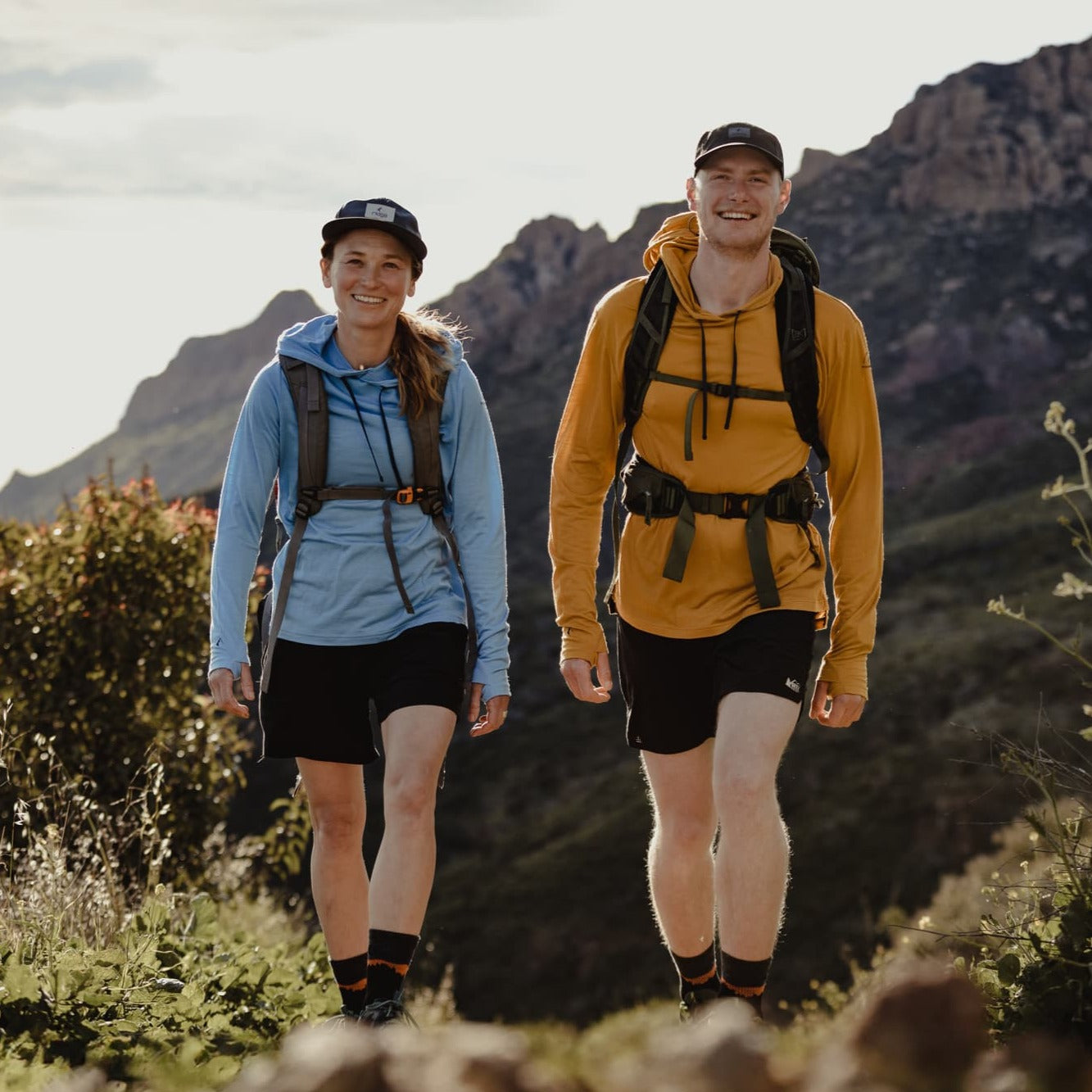 a woman and man walking on a trail wearing Ridge Merino Solstice Sun Hoodies and backpacks